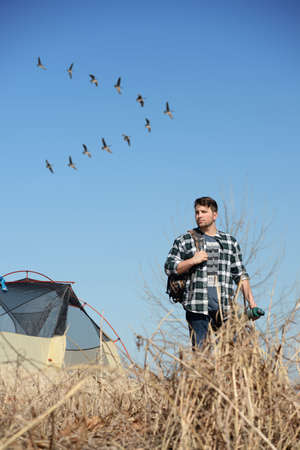 Young man camping while flock of geese fly in background