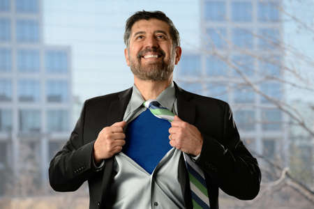 Mature Hispanic businessman opening shirt with office building in backgroundの写真素材