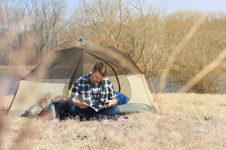 Young man reading seating outside camping tentの写真素材