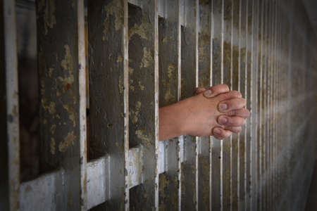 Hands of prisoner clenched resting on prison bars