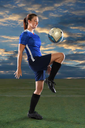 Female soccer player bouncing ball on knee at duskの写真素材