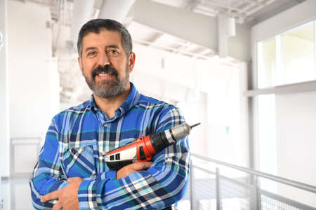 Hispanic man holding electrical drill inside building