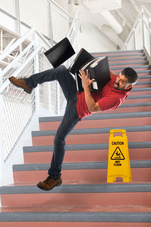 Hispanic businessman falling on stairs while carrying foldersの写真素材