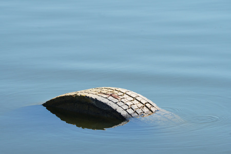 Tire in the water. Caused damage to the ecological environment of water area, by littering the coast. Old used tires lies in the sea. water blue background.の写真素材