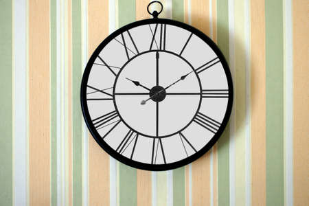 The close-up of a wall clock before a striped wallpaper                     