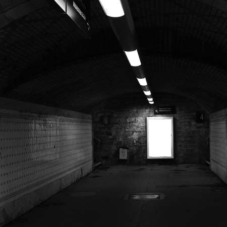 Dark railway station tunnel with artificial light and a poster frame                     