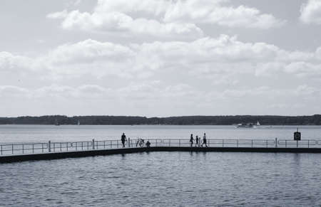 Waren, Mecklenburg Western Pomerania / Germany - June 9, 2013: Tourists walk on a concrete jetty with railings and look over the water of the Mueritz on June 09, 2013 in Waren.                 のeditorial素材