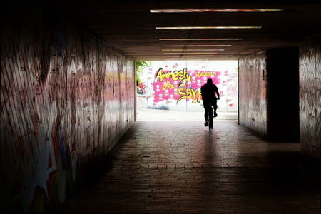 Under a bridge  the walls are painted with graffiti, and a cyclist travels through the tunnel                   のeditorial素材