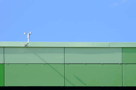 The photograph of the propeller of a wind sensor on the roof edge of a modern building