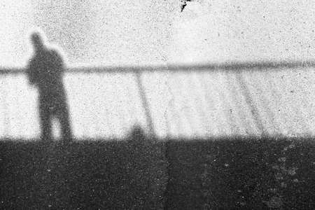 The silhouette of the shadow of a bridge and a man on the asphalt.