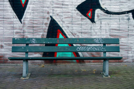 A park bench stands in front of a building with graffiti.の写真素材