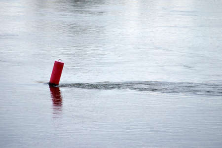 A red buoy is inclined from the river flow and forms a vortex behind it.の写真素材