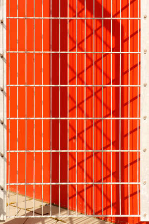 The fence in the sunshine raises a striking shade on a red facade.