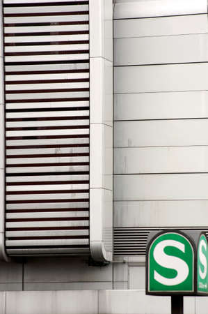 A green nostalgic tram sign stands in front of a striking facade made of metal.