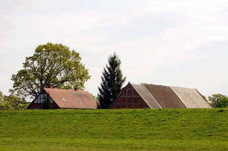 The roof of a barn and an apartment building behind a green dike.の写真素材