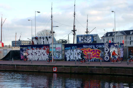 Amsterdam Netherlands 31 December 2014: Cyclists ride on the pier at the open waterfront in Amsterdam near Barracks with graffiti on December 31 2014 in Amsterdam.のeditorial素材