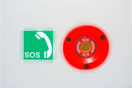 An emergency switch and an SOS sign sticker with a telephone receiver on the wall of a toilet for the disabled.の写真素材