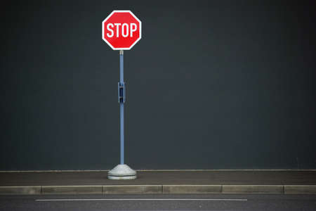 A stop sign stands in front of a homogeneous wall on a sidewalk.