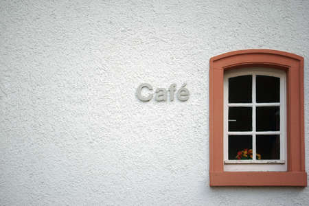 The facade of a coarse plastered cafe with a small window in which a flower vase stands.の写真素材