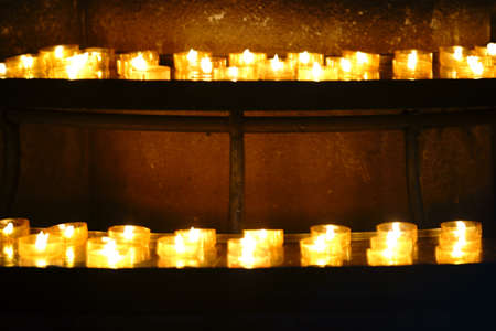 The closeup of prayer candles on two shelves and in a row.