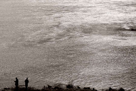 The silhouettes of two anglers standing in the evening light on a glittering river.の写真素材