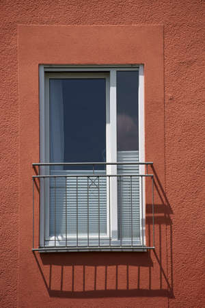 A railing in front of a window of a residential building casts a shadow.