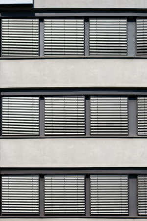 The modern facade of an office building with a row of windows and metal shutters.