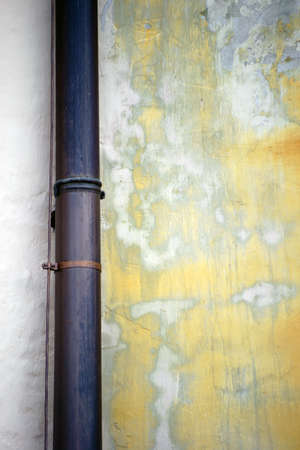 A rain of copper pipe is attached to a light wall with traces of water.