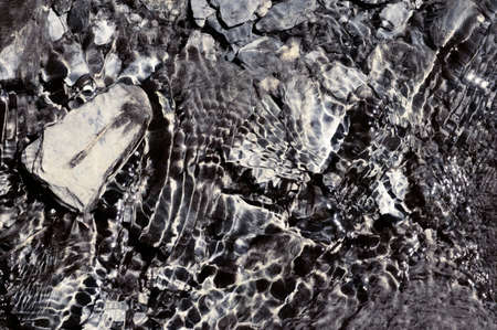 A stream with sediments, water plants and stones in clear sparkling water.