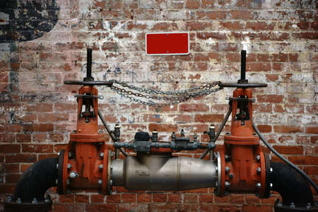 A pumping station is in front of an old brick wall with faded characters and color layers.