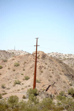 An electric pole stands in the middle of a barren desert landscape on a hillの写真素材