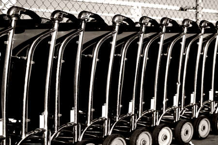 Baggage car of a luggage cart rental are consecutively ranked on the sidewalk and the entrance of an airport.の写真素材