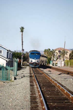 A train runs on a track in Oceanside between houses.