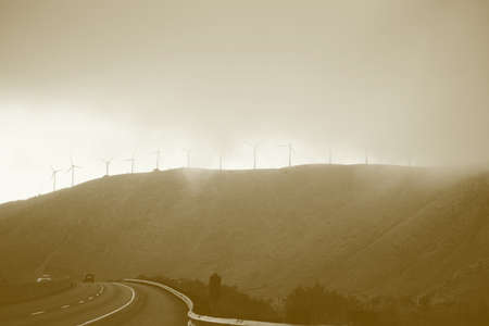 A road in the mountains with a windmill park on the mountainside in fog and with traffic.の写真素材
