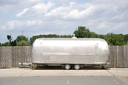 A round silver-colored caravan of sheet metal is parking on a wooden fence.