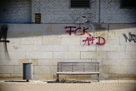 A park bench is on the facade of a building, which is scribbled with graffiti tags.の写真素材
