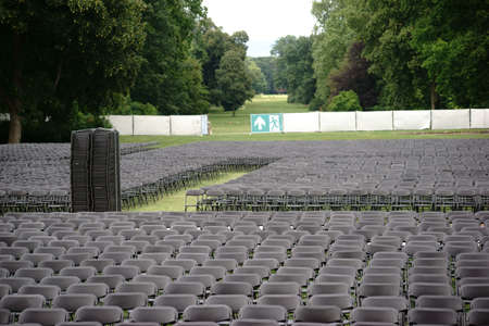 Parallel arranged empty seat rows of folding chairs on a lawn of an open-air concert with an...