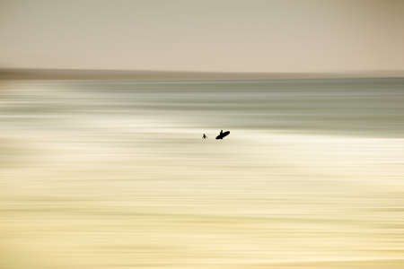 The blurred sea at Oceanside with silhouettes of surfers in the water.の写真素材
