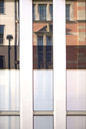 Abstract reflections of buildings and street lanterns in tall and narrow windows of a modern...