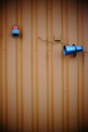 An old, battered speaker and a warning light on a corrugated iron wall                             の写真素材
