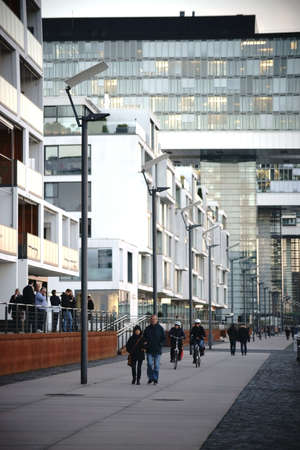 Cologne, Germany - November 24, 2016: Pedestrians walking and cyclists ride in the evening along the Rhine promenade on the crane houses on November 24, 2016 in Cologne.のeditorial素材