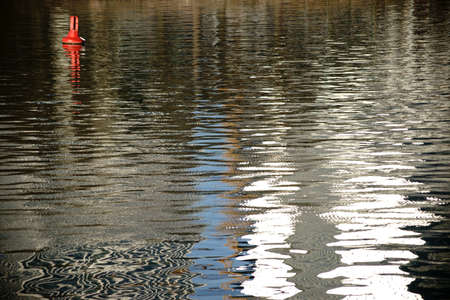 A red signal buoy floats on the abstract water surface of a river.                         の写真素材