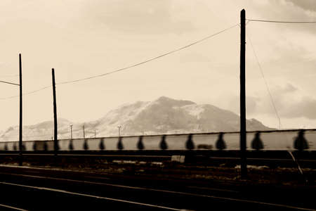 A blurred freight train and tracks next to the main road in Mojave city with mountains in the background.の写真素材