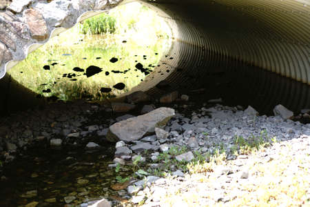 The top view and close-up on the stones of a rubbish bed of a pond under a tubular bridge underpass.                         の写真素材