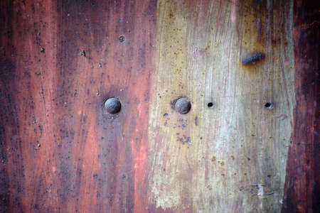 The closeup of a rusty metal surface with rust bubbles and rusty rivets.
