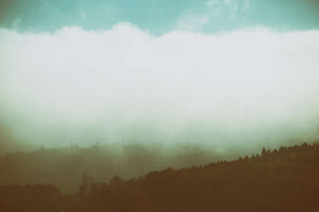 Clouds and fog pass over the wooded ridges of a mountain chain.                            の写真素材