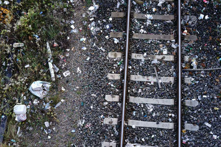 The top view of a track bed with rails and ballast stones and a lot of trash and garbage.           ...
