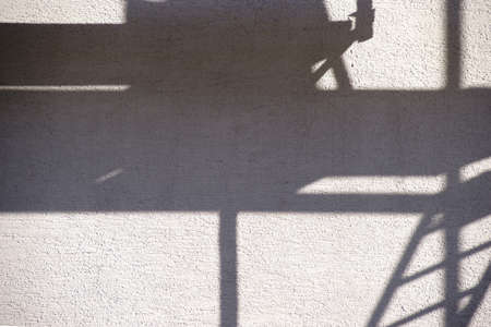 The Pipes and wooden inserts from a scaffolding cast abstract shadows on a wall.