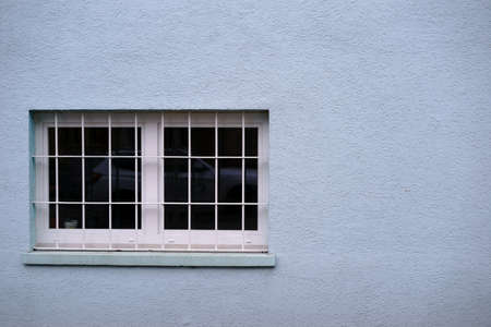 The detail of a lattice window on the plastered house facade.                         