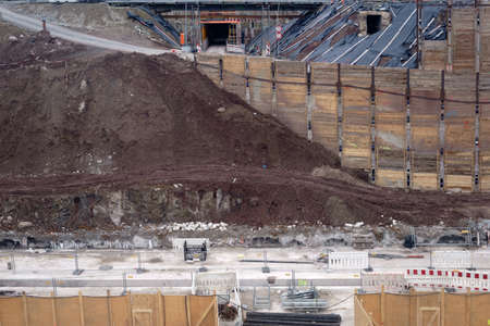 The side view of a excavated and fortified excavation of a construction site with worn and heaped up sand piles of earth.                         の写真素材